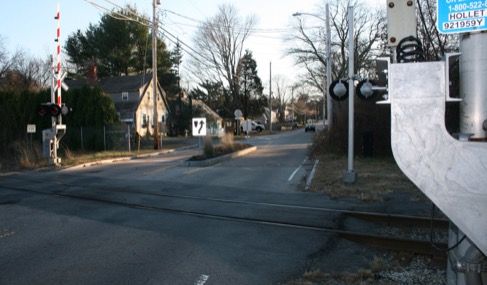This figure is an image showing crossing gates protecting a road where the Greenbush commuter rail line crosses. A residential area is on the far side of the tracks.
